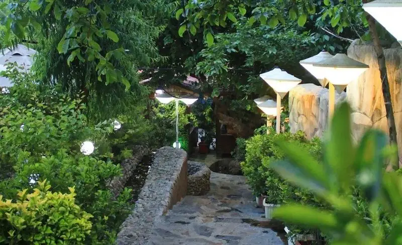 باغ رستوران سایدا شهران: مسیر سنگی زیبا، درختان سرسبز، نورپردازی دلنشین و فضایی آرام برای تجربه غذایی لذت‌بخش در شب.