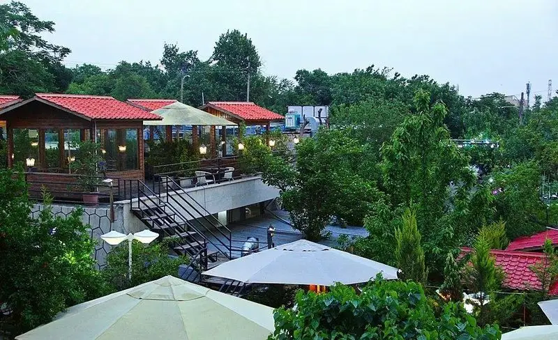 باغ رستوران سایدا شهران، نمایی دلنشین از آلاچیق‌های چوبی سقف قرمز، تراس سرسبز و محیطی آرام برای صرف غذا در فضای باز.