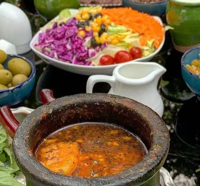 نمایی جذاب از میز غذا در باغ رستوران سایدا شهران: سالاد متنوع، خوراک سنتی در دیگ سفالی، زیتون و محیط دلنشین برای ناهار و شام.