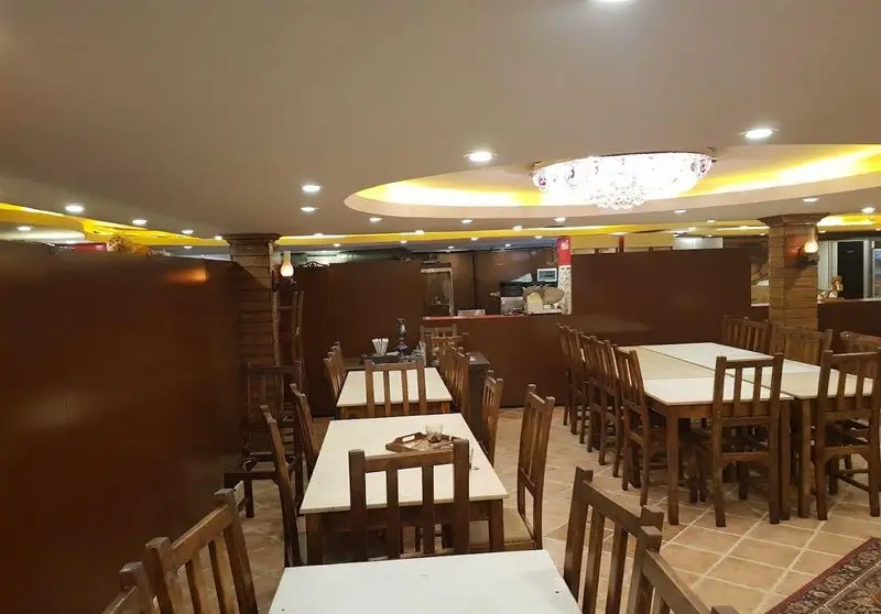 فضای داخلی زیبا و دنج رستوران و خدمات مجالس سیمرغ، با میز و صندلی‌های چوبی، نورپردازی گرم و سقفی مدرن و شیک.