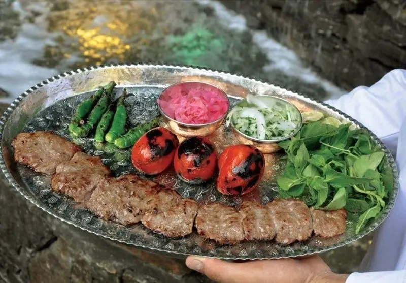سینی کباب کوبیده لذیذ کبابی سلطانی شعبه 1 با گوجه، فلفل، سبزی تازه و ترشی در کنار رودخانه، غذای اصیل ایرانی.