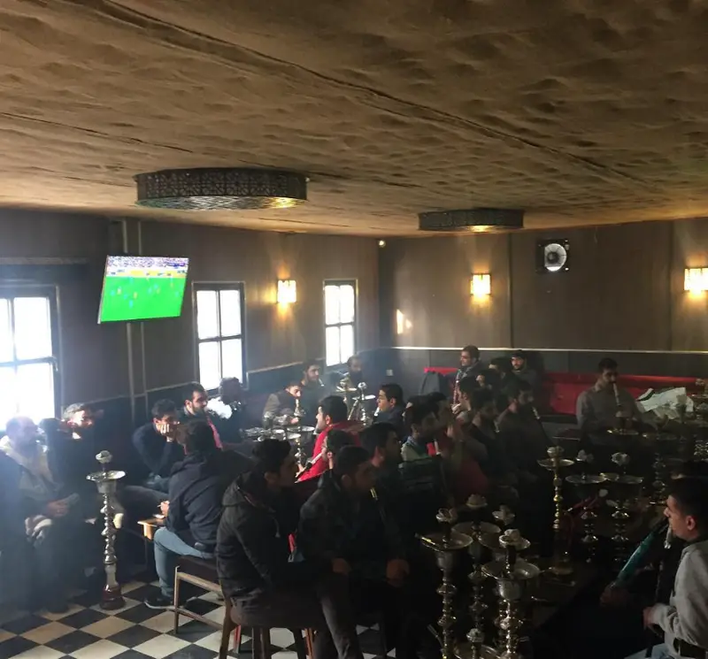 کافه مافه: تصویری از مشتریان مرد در حال تماشای فوتبال روی صفحه نمایش بزرگ، لذت بردن از کشیدن قلیان و دورهمی صمیمی در فضای دنج و دلنشین.