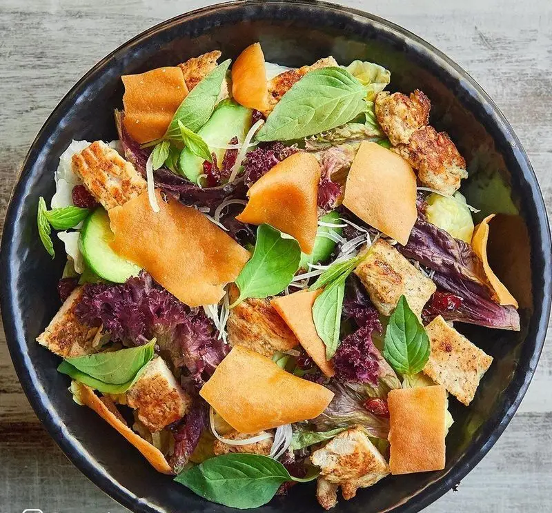 سالاد جذاب و کامل باروژ: مرغ گریل، کاهو، خیار، نان کریسپی، سبزیجات تازه و دانه‌های انار. گزینه‌ای سالم از منوی فست فود.