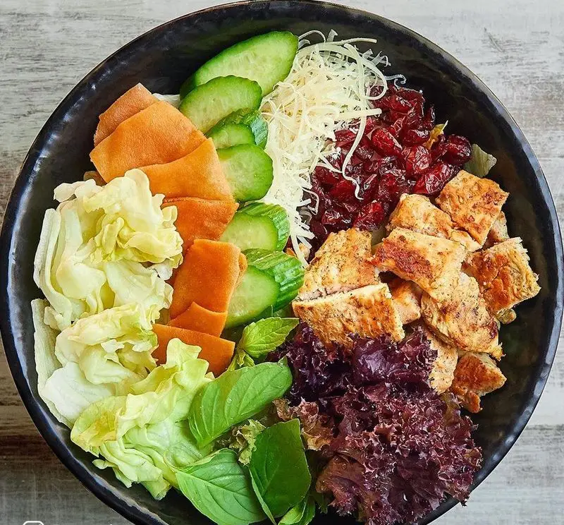 تصویری از یک کاسه سالاد رژیمی و رنگارنگ با تکه‌های مرغ، کرنبری، پنیر، کاهو و سبزیجات تازه از فست فود باروژ.