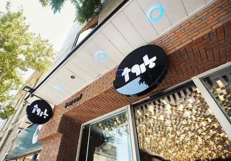 نمای بیرونی فست فود باروژ با تابلوی شیک مشکی، دیوارهای آجری و نورپردازی آبی مدرن. طراحی جذاب ورودی رستوران در فضای شهری.