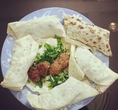 بشقاب فست فود پاتوق با رول‌های نان تازه حاوی کباب‌های خوشمزه گوشت و سبزیجات معطر، آماده برای یک وعده غذایی لذیذ و پرطرفدار.