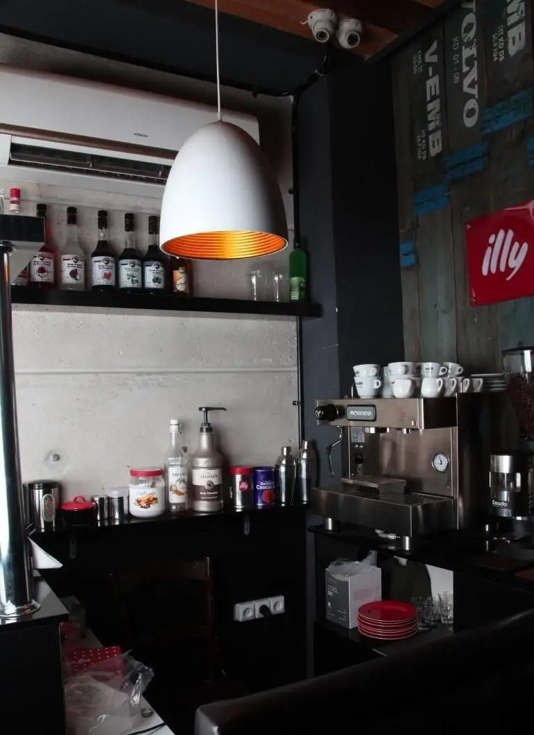 فضای داخلی کافه رستوران چاپ چاپ (فرشته): کانتر با دستگاه اسپرسو، سیروپ های متنوع، فنجان قهوه، تابلوی ایلی و دکوراسیون شیک و مدرن.