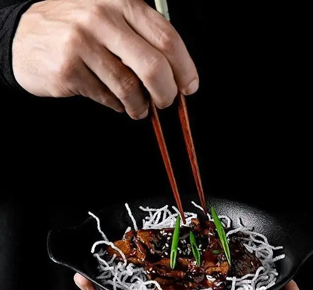 تصویری از غذای محبوب رستوران چاپ چاپ فرشته: برش‌های گوشت در سس تیره، روی نودل سفید ترد، با تزیین پیازچه و کنجد، آماده برای صرف با چاپستیک.