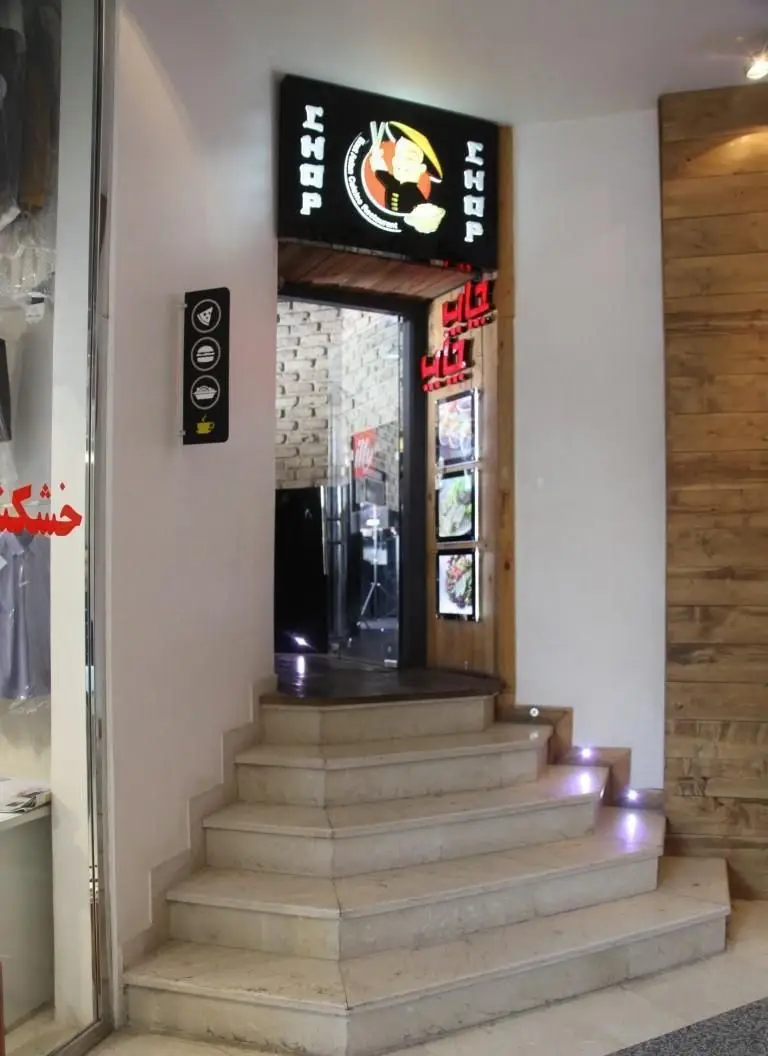 ورودی مدرن رستوران چاپ چاپ فرشته با پله‌های سنگی و تابلو CHOP CHOP، نمایشگرهای غذا و دکور چوبی جذاب.