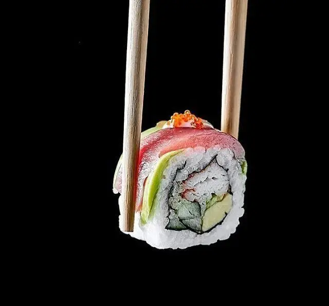 یک رول سوشی دست‌ساز و تازه با تکه‌های ماهی تن، آواکادو و تاپینگ خاویار که با ظرافت با چاپستیک نگه داشته شده. رستوران چاپ چاپ فرشته.