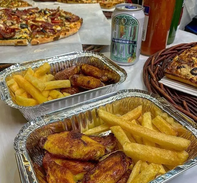 پیتزا کوک: وعده غذایی فست فود شامل بال سوخاری و سیب زمینی سرخ کرده تازه در بسته بندی بیرون بر، کنار پیتزا خوشمزه و نوشیدنی مالت.