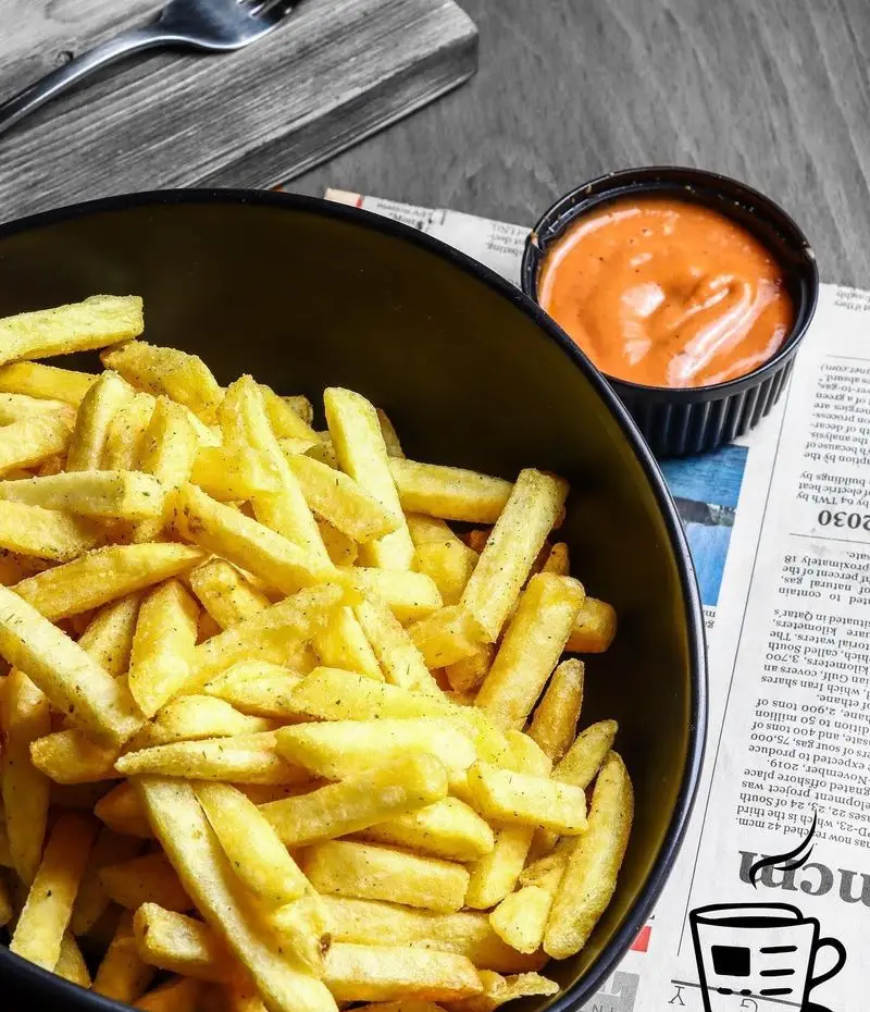 کاسه‌ای پر از سیب‌زمینی سرخ کرده داغ و خوشمزه کافه لید با سس مخصوص کنار روزنامه. بهترین انتخاب برای یک وعده یا میان‌وعده عالی.