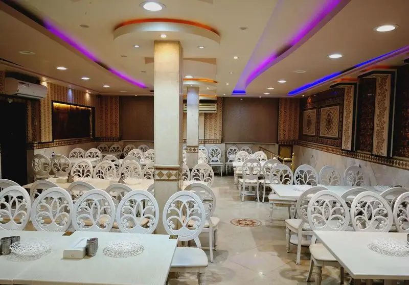 سالن دلباز کبابی گلبرگ با میز و صندلی‌های سفید زیبا و خاص، دکوراسیون مدرن و نورپردازی بنفش و آبی دلنشین، محیطی تمیز و آماده پذیرایی.