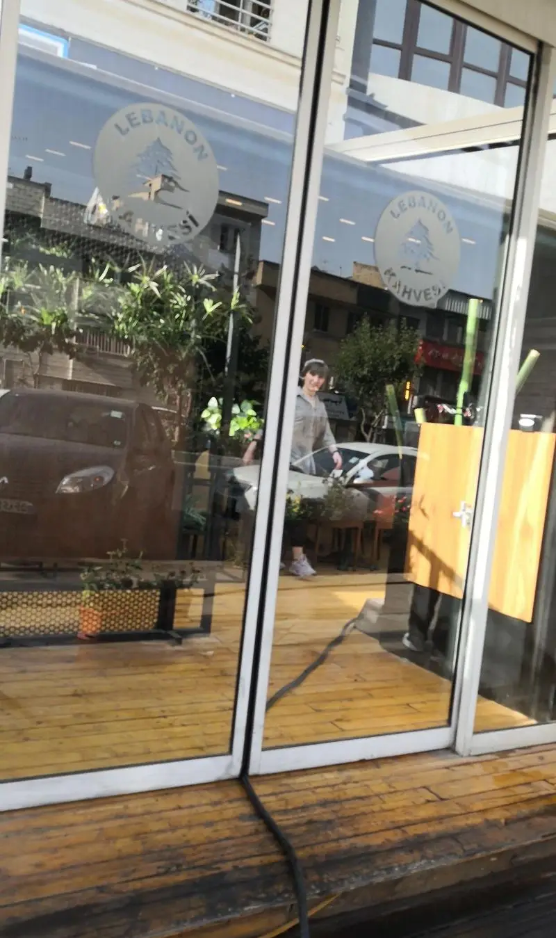 نمایی جذاب از کافه لبنان، با لوگوی درخت سرو لبنانی بر روی شیشه، دکوراسیون چوبی گرم و محیطی دلنشین برای قهوه و نوشیدنی.