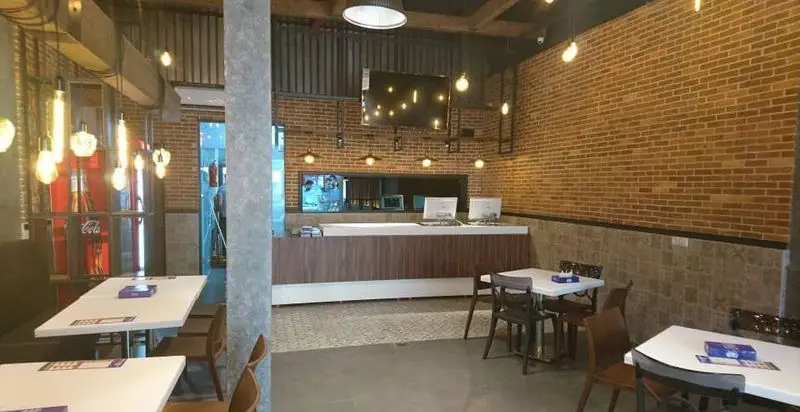 محیط داخلی دلنشین و مدرن پیتزا سیب ۳۶۰ با دیوار آجری، میز و صندلی‌های راحت و کانتر سفارش. فضایی ایده‌آل برای لذت بردن از غذا.