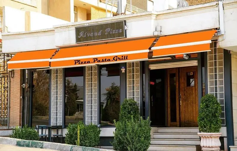 نمای بیرونی جذاب رستوران پیتزا الوند با سایبان‌های نارنجی، ورودی چوبی، و علائم "Pizza.Pasta.Grill" برای جذب مشتریان.