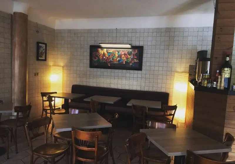 محیط دلنشین و مدرن پیتزا الوند، با چیدمان میز و صندلی‌های راحت، دیوار کاشی، نقاشی رنگی، نورپردازی گرم و کانتر خدمات، ایده‌آل برای دورهمی.