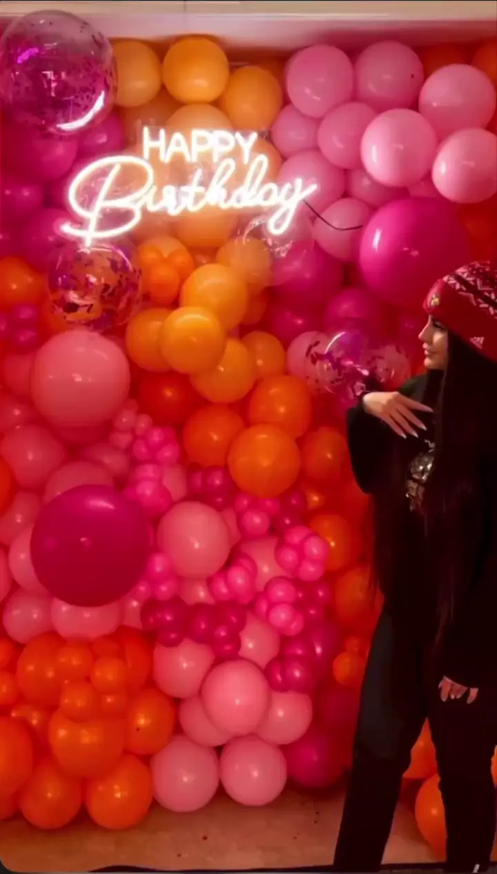 دکور بالون تولد شاد و رنگارنگ برای جشن‌های خاص، شامل دیوار بالونی صورتی و نارنجی با تابلو نئون Happy Birthday، دیزاین حرفه‌ای بالونیا.