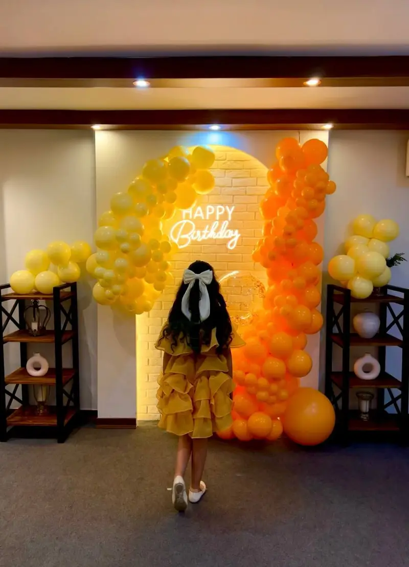 بادکنک آرایی شیک و دیزاین تولد با تم زرد و نارنجی، همراه با تابلو نئون Happy Birthday، از خدمات بالونیا.