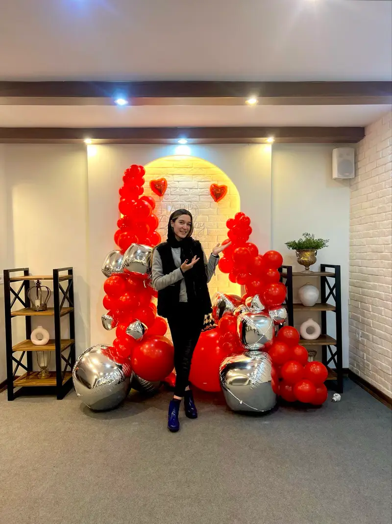 دیزاین بالون و بادکنک آرایی قرمز و نقره ای شیک برای جشن و مراسم در بالونیا. دکوراسیون تولد با قلب و نورپردازی.