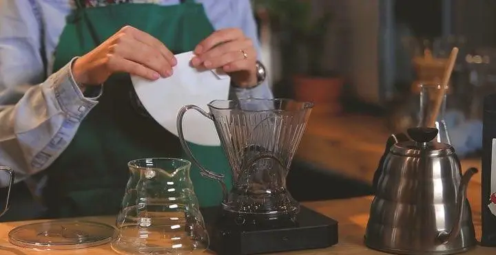 آماده سازی حرفه‌ای قهوه دمی در کافه رئیس توسط باریستا با استفاده از فیلتر و ابزار مدرن برای تجربه طعمی بی‌نظیر.