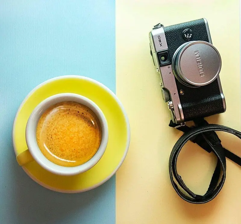اسپرسو تازه با کرمای طلایی در فنجان زرد کافه رئیس، کنار دوربین فوجی فیلم X20 نقره‌ای. لحظات دلنشین عکاسی و قهوه.