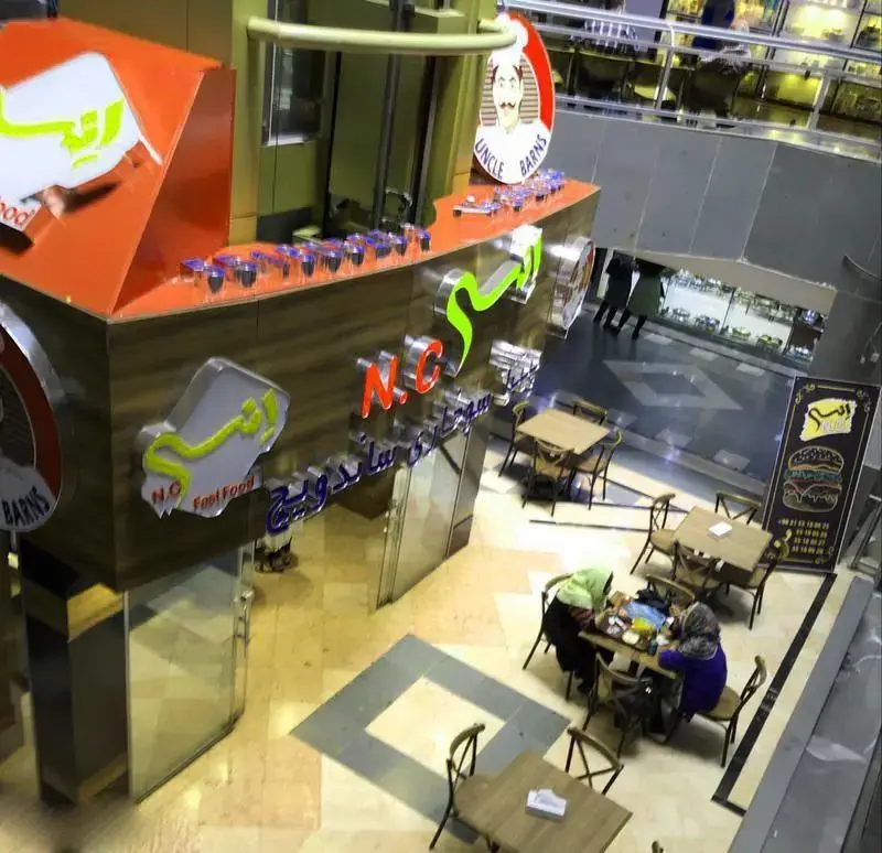 نمای چشم‌انداز فست فود انسی، با لوگوی نئونی و چیدمان میز و صندلی‌های شیک. محیطی عالی برای تجربه لذیذترین ساندویچ‌ها و برگرها در فودکورت.