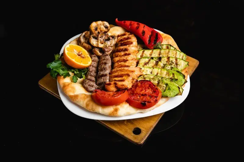 بشقاب گریل کافه گریل ببک شامل کباب کوبیده، جوجه گریل، سبزیجات کبابی (قارچ، کدو، گوجه، فلفل) و نان تخت. غذای خوشمزه و سالم.