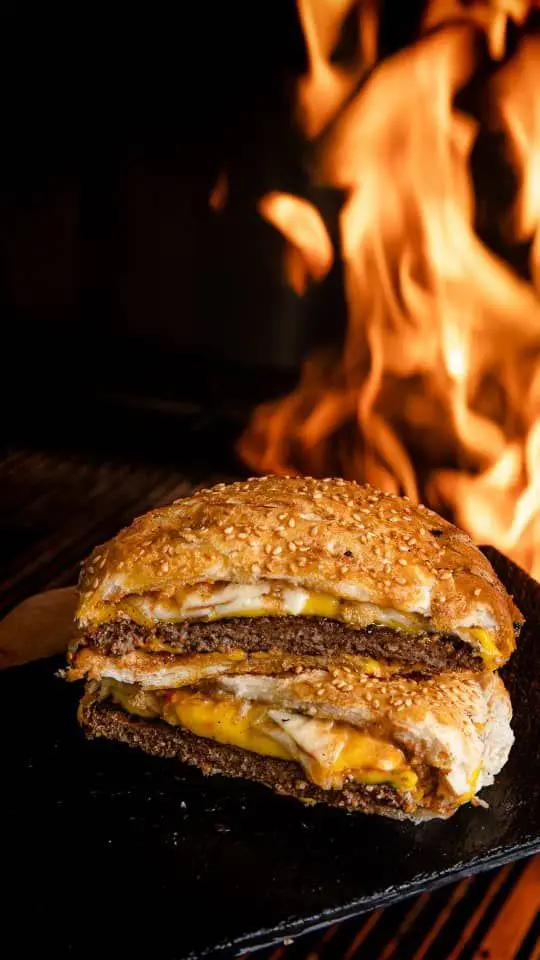 برگر گریل شده لذیذ کافه گریل ببک با پنیر ذوب شده و نان کنجدی، در پس زمینه شعله های آتش. یک غذای گریل خاص و خوشمزه.