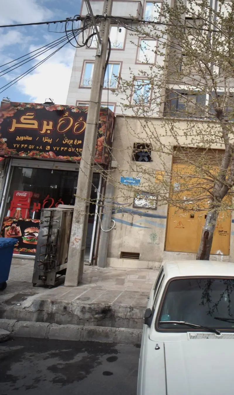 نمای بیرونی فست فود Oُ Oُ برگر با منوی مرغ بریان، پیتزا و ساندویچ در خیابانی شلوغ، شامل تیر برق و خودروی سفید.