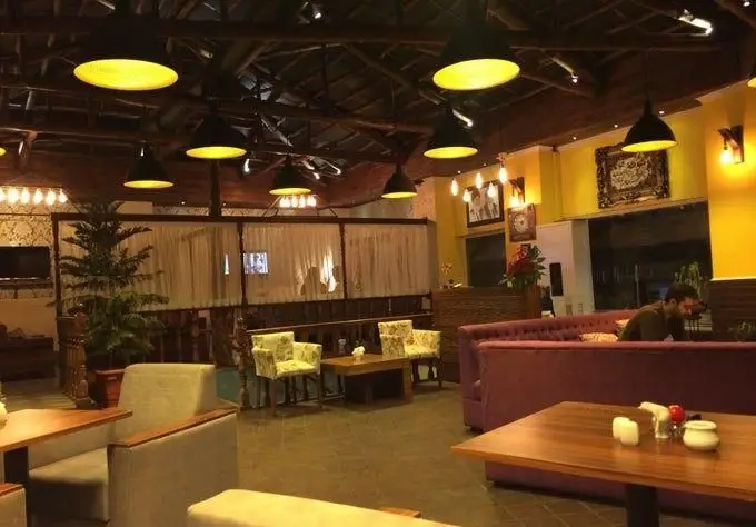 تصویر فضای داخلی سرای سنتی دفینه با سقف چوبی، مبلمان راحت بنفش و میز و صندلی‌های سنتی، نورپردازی گرم و محیطی دلنشین.