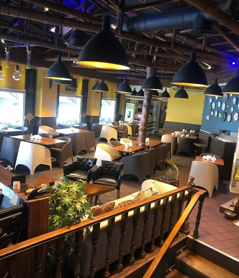 نمای داخلی زیبای سرای سنتی دفینه با دکوراسیون چوبی، لوسترهای آویز و چیدمان گرم و دلنشین میز و صندلی در محیطی آرام.