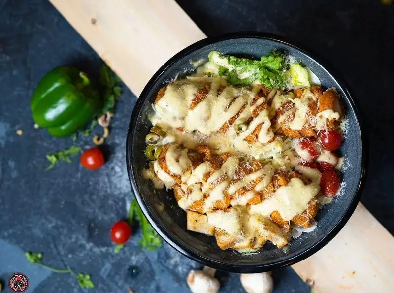 غذای اصلی لذیذ کافه رستوران ایتالیایی دیبارو: یک کاسه پر از مرغ سوخاری با سس خامه ای، پنیر پارمزان، گوجه گیلاسی و کاهو تازه.