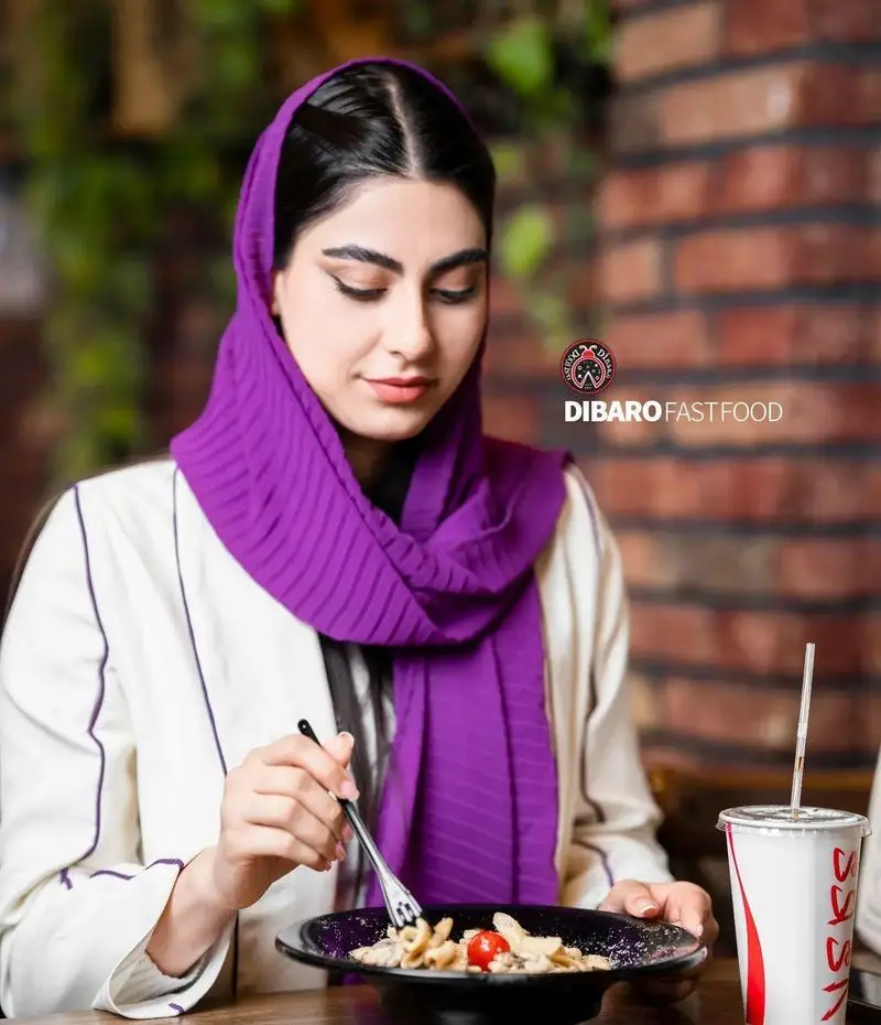 زن جوان با حجاب بنفش در کافه رستوران ایتالیایی دیبارو، از خوردن پاستای خوشمزه لذت می‌برد. مکانی عالی برای غذای ایتالیایی.