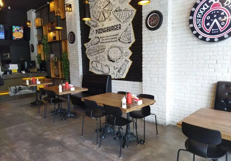 نمای داخلی کافه رستوران دیبارو: دکوراسیون صنعتی-مدرن، میزهای چوبی، صندلی‌های راحتی، دیوار آجری سفید و نقاشی بزرگ پیتزا و برگر.