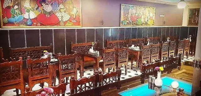 فضای رستوران سنتی انتظامی با چیدمان میز و صندلی‌های چوبی منبت‌کاری شده، نقاشی‌های اصیل و محیطی گرم و دعوت‌کننده.