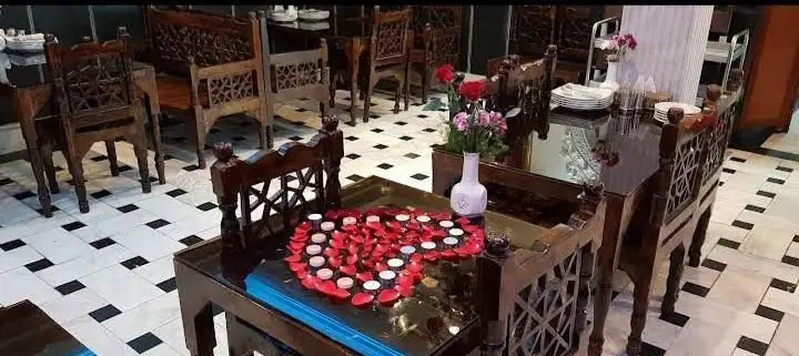 فضای رمانتیک رستوران انتظامی با میز و صندلی‌های چوبی منبت‌کاری شده، تزیین قلب با گلبرگ و شمع برای لحظات خاص و به یادماندنی.