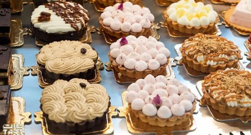 نمای نزدیک از انواع تارت‌های تازه و لذیذ شیرینی فروشی تارت، شامل دسرهای کرمی، مرنگ و مغزدار با تزئینات خاص.
