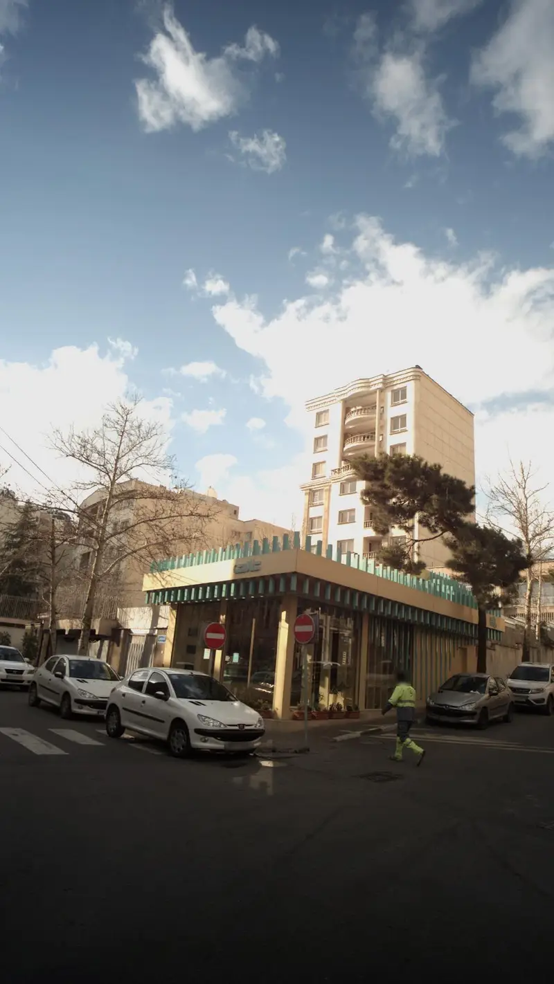 تصویری از خیابان و نمای بیرونی شیرینی فروشی تارت با معماری خاص، خودروهای پارک شده و آسمان صاف. مکانی دلپذیر برای تجربه طعم شیرین.