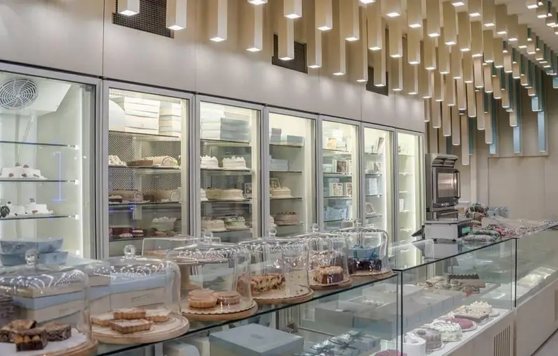 دکوراسیون داخلی شیک شیرینی فروشی تارت، با ویترین‌های پر از کیک، تارت، دسر و شیرینی‌های تازه. فضای مدرن و نورپردازی زیبا.