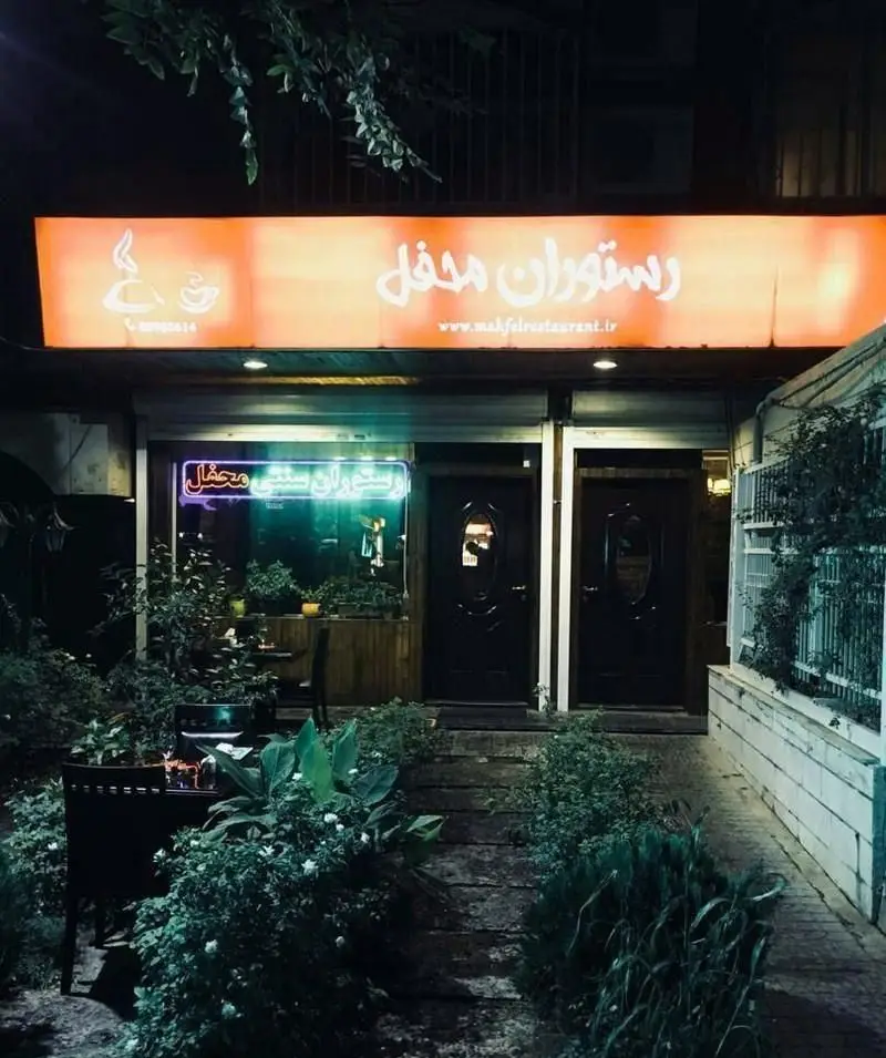 نمای بیرونی و ورودی دلنشین رستوران ایرانی سنتی محفل در شب با نورپردازی گرم، فضای سبز زیبا و محیطی دلپذیر.