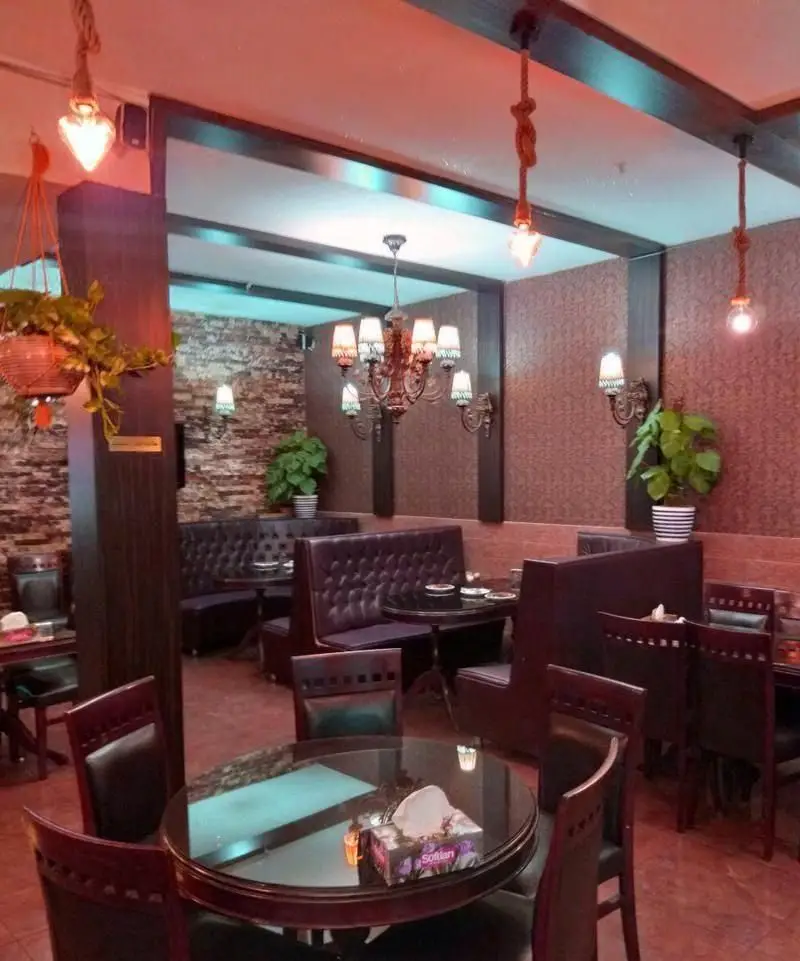 فضای داخلی دنج و شیک رستوران ایرانی محفل با میز و صندلی‌های راحت، لوسترها، گلدان‌ها و دکوراسیون سنتی و مدرن.