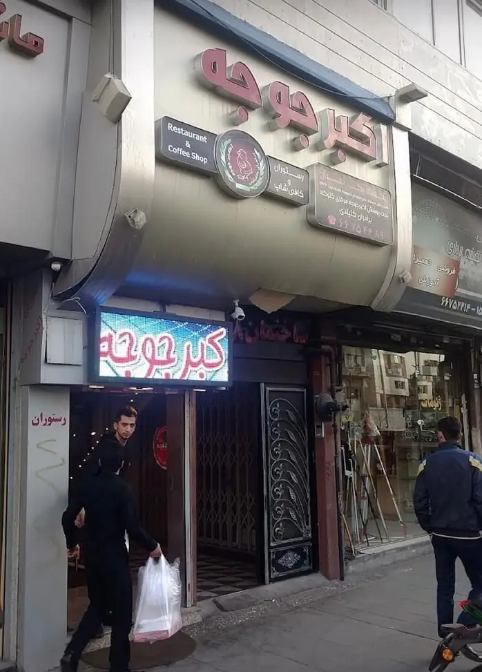 نمای بیرونی رستوران و کافی شاپ اکبر جوجه با تابلوی مشخص و مشتری در حال خروج، مکانی ایده‌آل برای غذای تازه و بیرون بر.