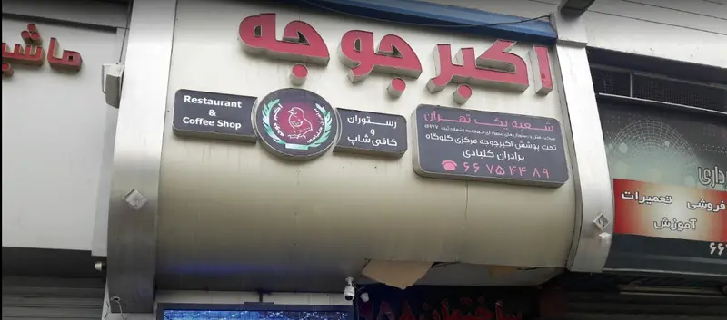 تابلو نمای بیرونی رستوران و کافی شاپ اکبر جوجه شعبه یک تهران با لوگوی مرغ و اطلاعات تماس ۶۶۷۵۴۴۸۹، متخصص غذای اصیل ایرانی.