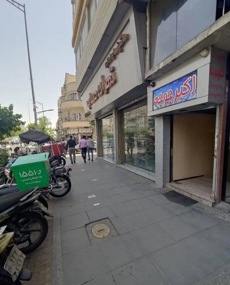 نمای بیرونی رستوران اکبر جوجه، عرضه کننده غذای ایرانی، با تابلوی LED و موتورهای آماده ارسال غذا در پیاده‌روی شلوغ شهری.