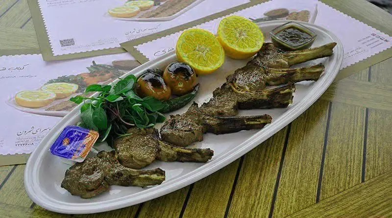 شیشلیک لذیذ شمرون کباب با لیمو تازه، گوجه کبابی، فلفل سبز و سبزی روی میز چوبی رستوران شمرون کباب.