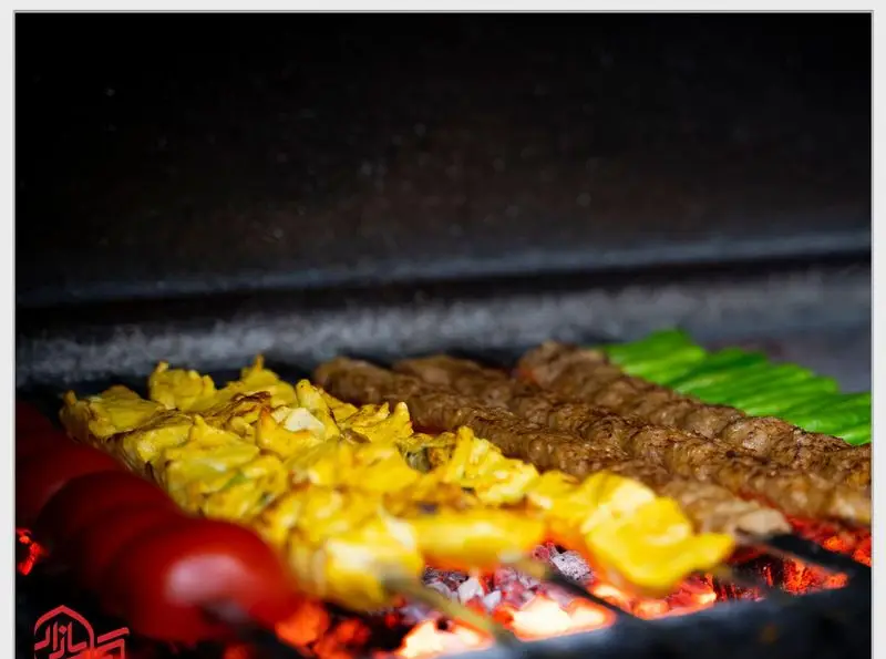 انواع کباب تازه و لذیذ شامل جوجه کباب زعفرانی و کباب کوبیده گوشت، در حال پخت روی منقل کباب بازار با زغال گداخته.