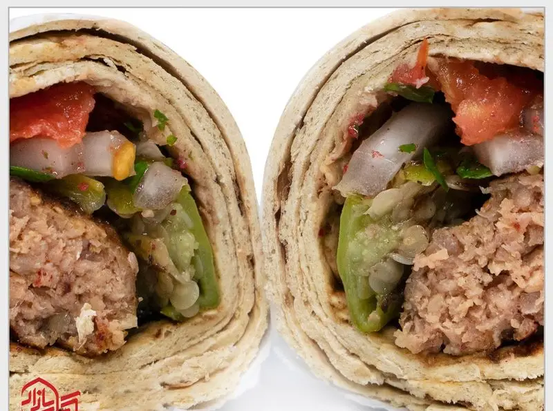 یک لقمه کباب کوبیده تازه و خوش‌طعم از "کباب بازار" که از وسط نصف شده، با کباب، گوجه، پیاز و سبزیجات معطر در نان سنتی.