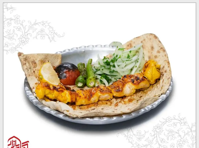 جوجه کباب لذیذ کباب بازار بر روی نان داغ، همراه با گوجه کبابی، فلفل سبز، پیاز و جعفری و برش لیمو تازه.