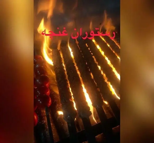 کباب کوبیده و گوجه کبابی داغ در حال پخت بر روی منقل ذغالی با شعله‌های آتش جذاب در رستوران غنچه، بهترین انتخاب برای غذای اصیل ایرانی.